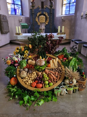 vor dem Altar liegt ein altes Wagenrad, innerhalb und außerhalb liegen verschiedene Sorten Gemüse, Nüsse, Getreide und Blumen schön angeordnet